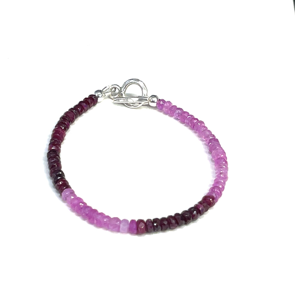 One genuine ruby gemstone beaded bracelet with sterling silver toggle clasps, featuring faceted round rubies ranging from pink to red on a white background, front overview.