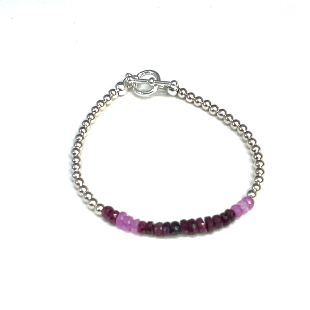 One genuine ruby gemstone beaded bracelet with sterling silver toggle clasps, featuring faceted round rubies ranging from pink to red with sterling silver beads, on a white background, front overview.