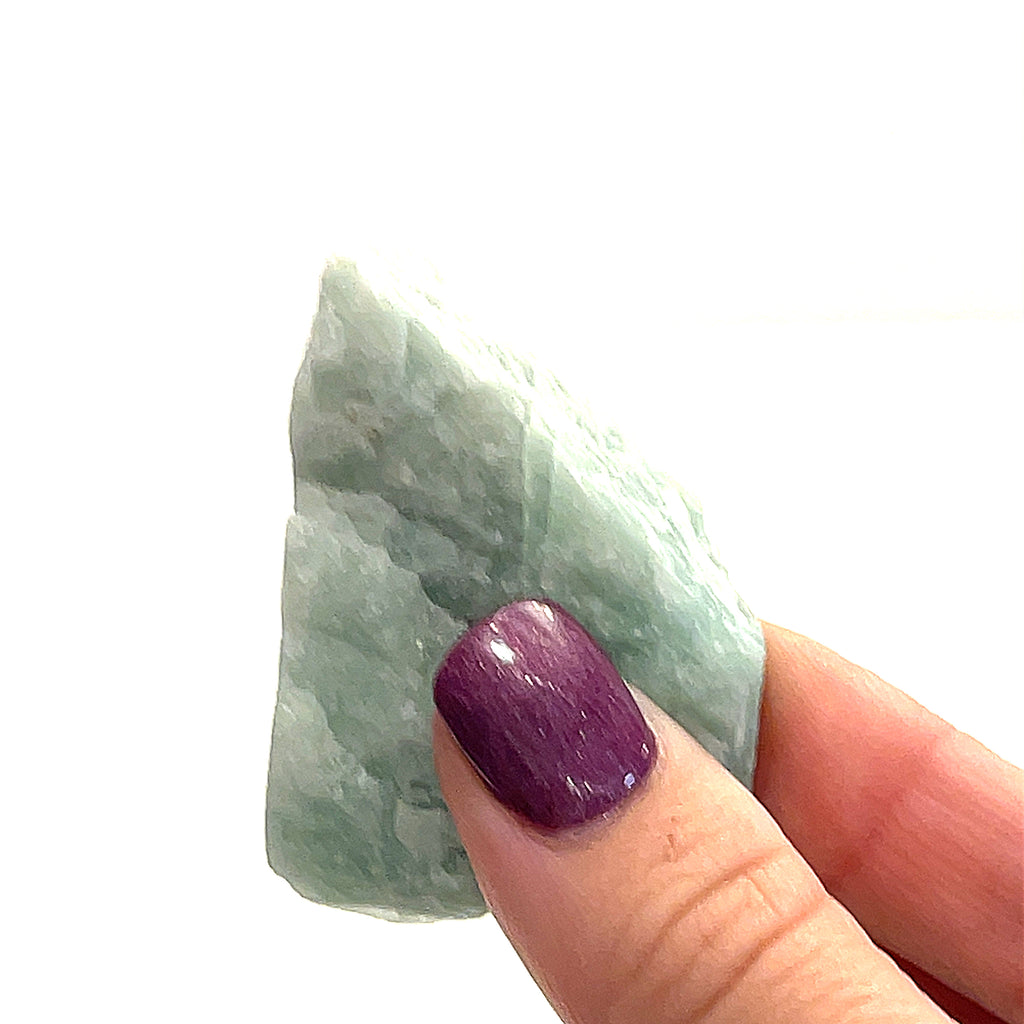 One raw Amazonite gemstones is displayed in a models finger tips on a white background, in front, in an overview. 