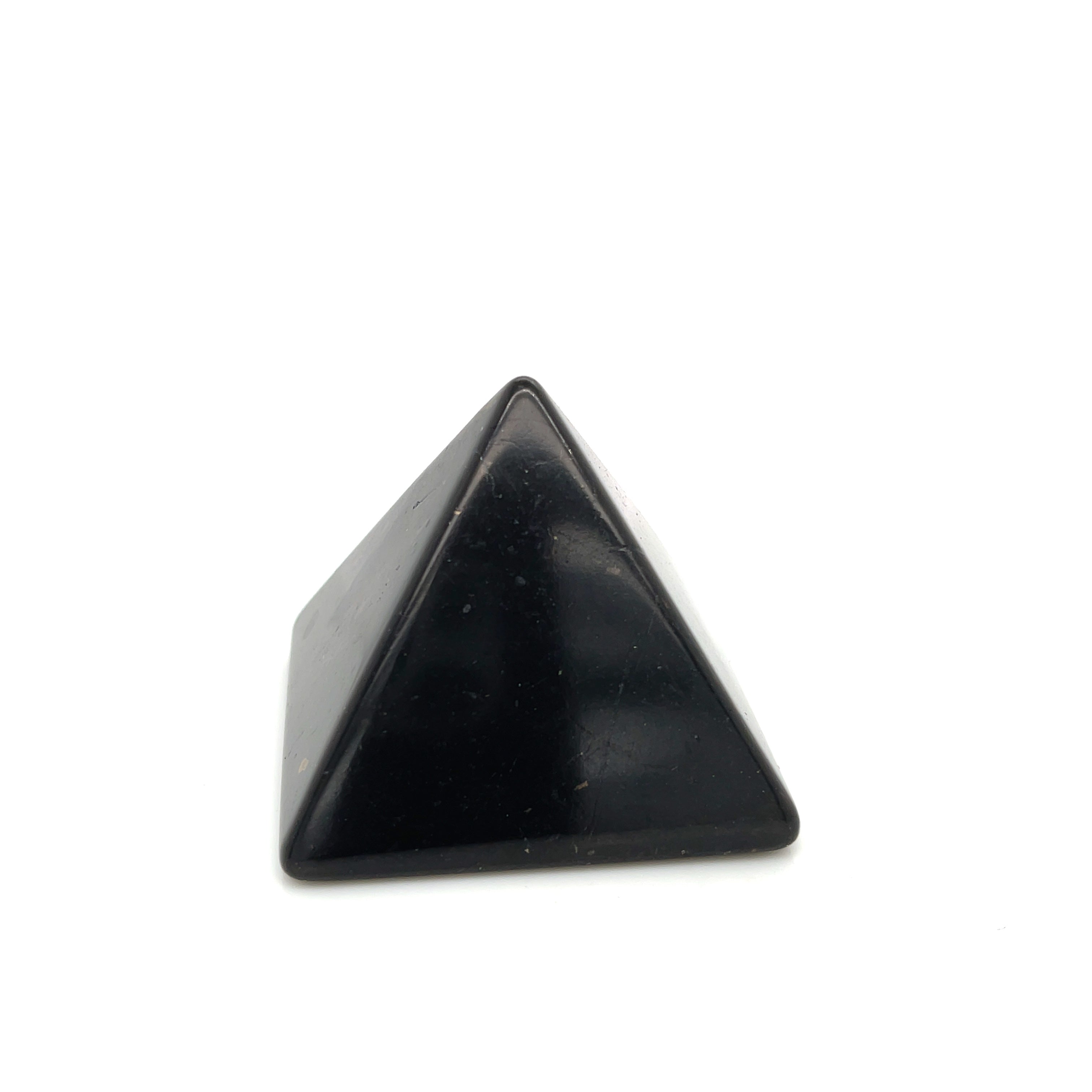 One small shungite pyramid on desk near computer for radiation blocking on a white background, front view. 