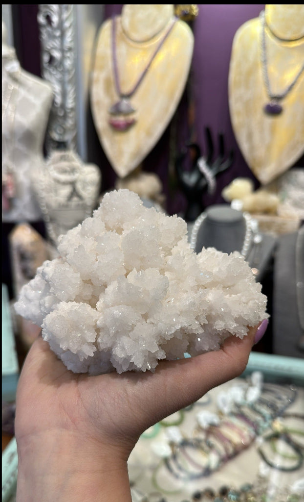Rare White Aragonite cluster from Chihuahua, Mexico showing raw crystalline texture. in models hand to show size with purple background front view.