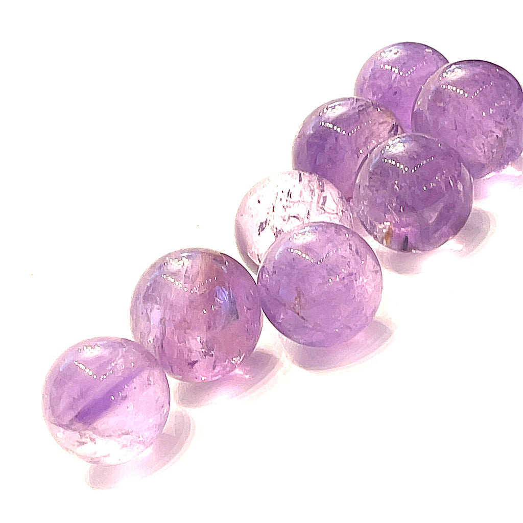  Several small purple amethyst gemstone spheres on a white background, front close-up overview. 