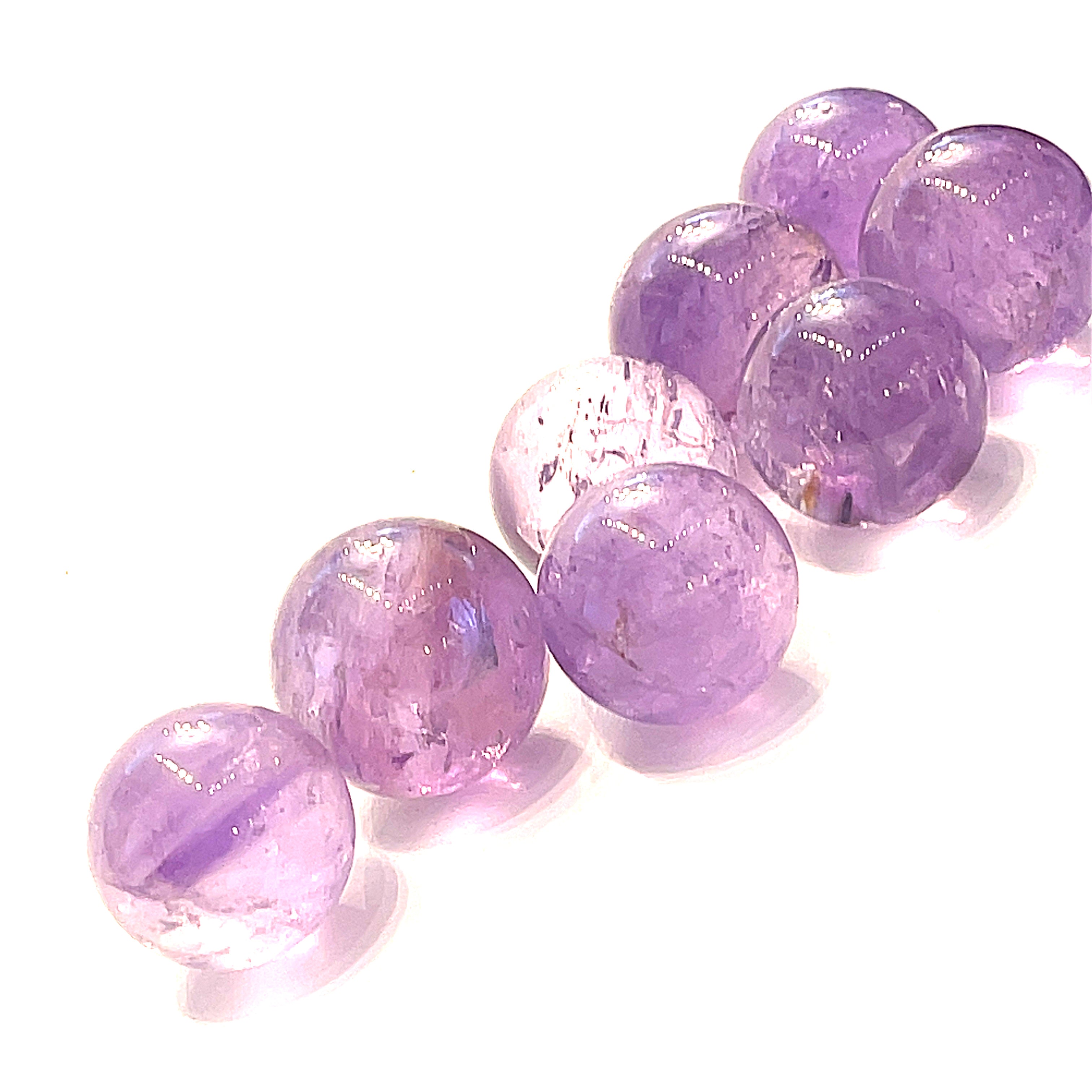  Several small purple amethyst gemstone spheres on a white background, front close-up overview. 