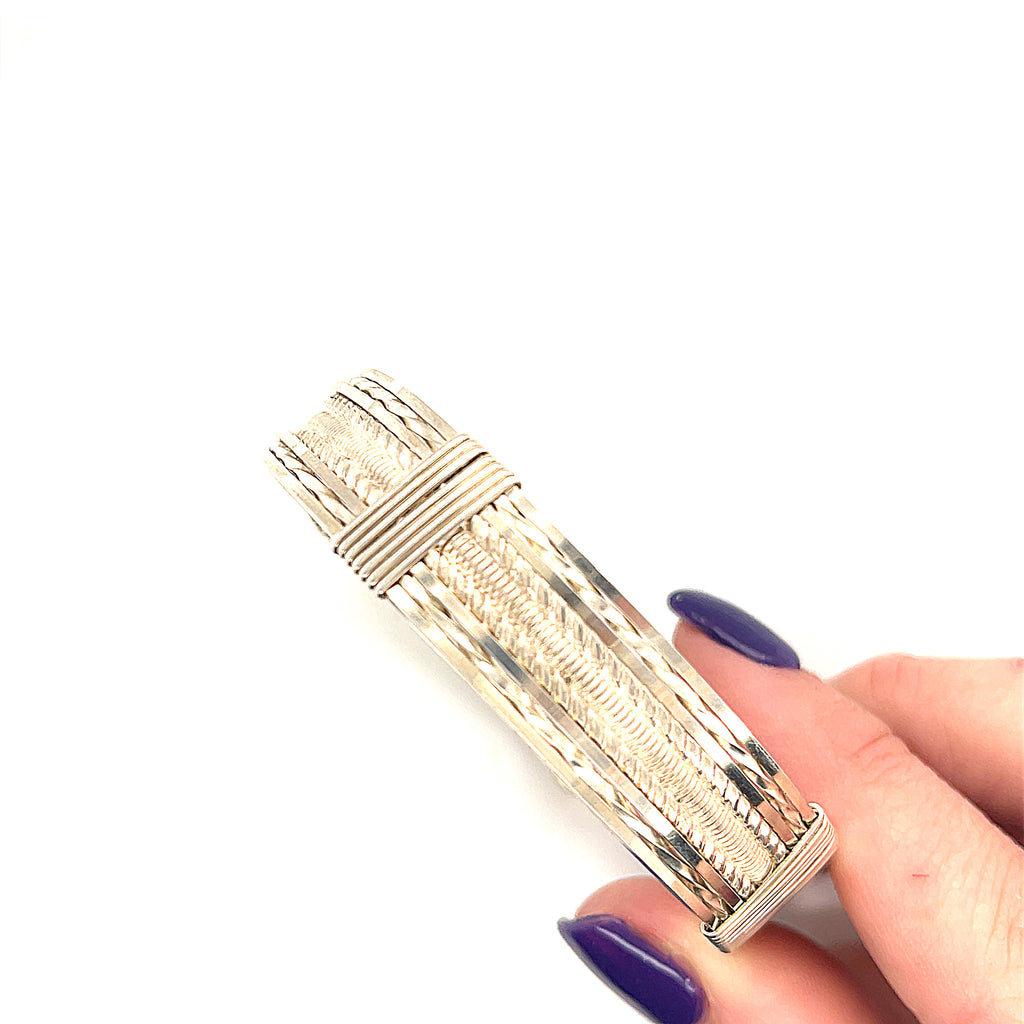 Style #1 Handcrafted sterling silver wire-wrapped bangle with twisted and straight wire combination showing polished dome centerpiece, on a white background in the model's hand, front view. 