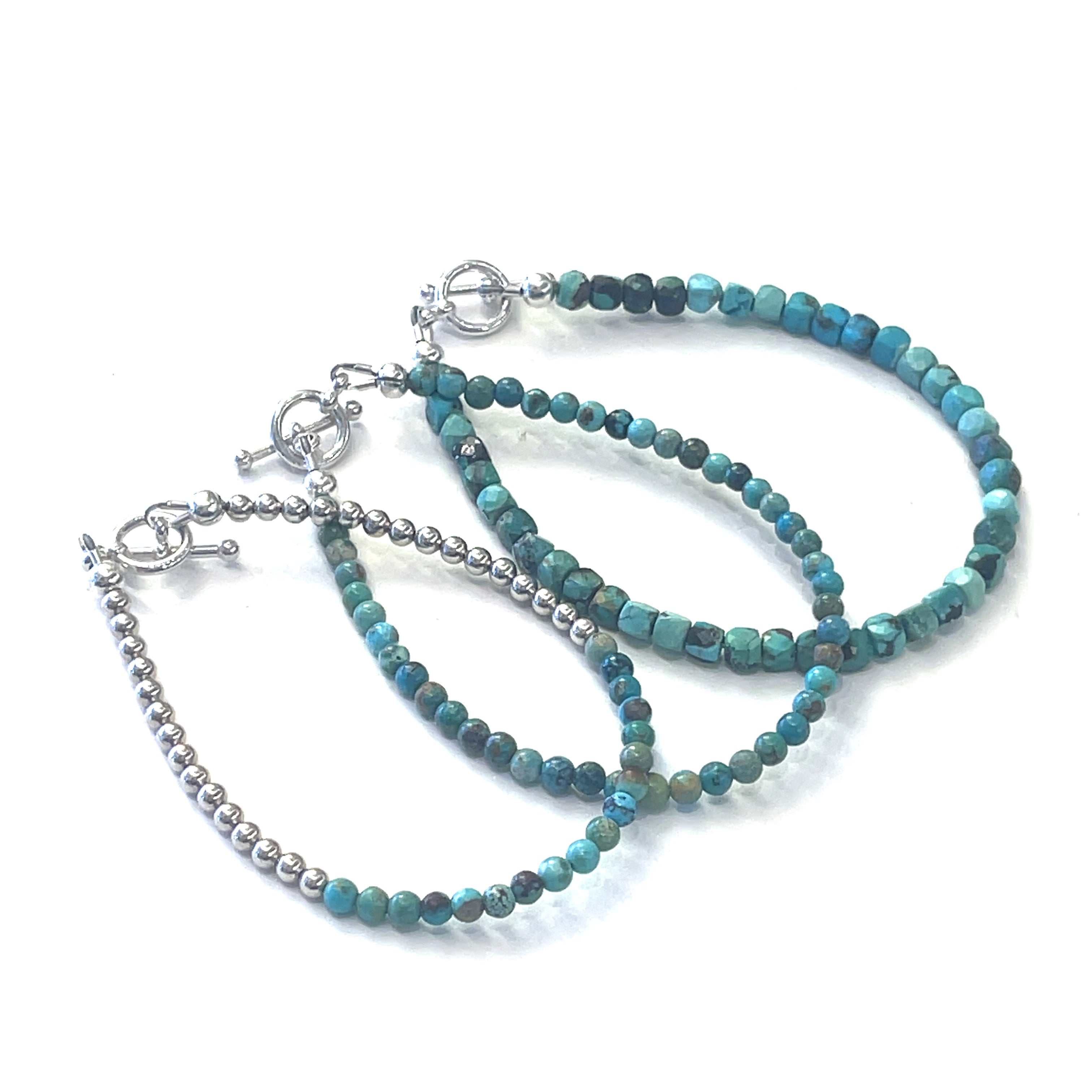 Three beaded gemstone bracelets with natural turquoise stones, strung on silver-colored cord with sterling silver toggle clasps on a white background front overview. 