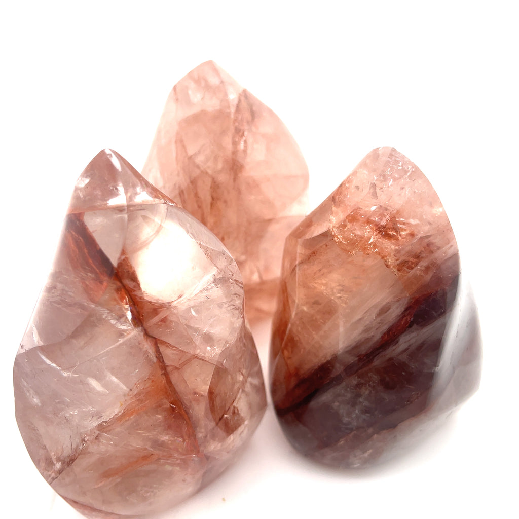 Three polished Fire Quartz gemstones with a flame-like carving and a pink to red gradient on a white background front overview.