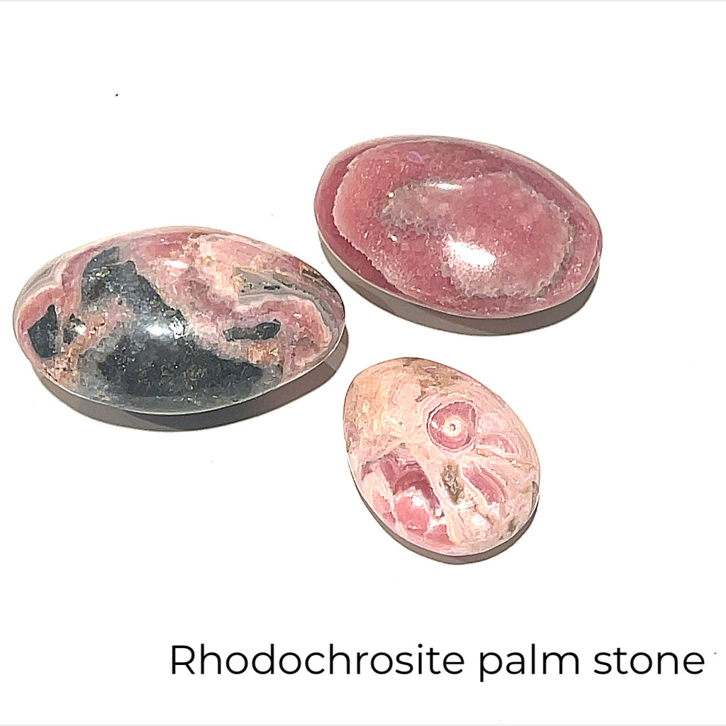Three polished Rhodochrosite gemstone palm stones with varying shades of pink to pale brown colors and white streaks on a white background front overview. 
