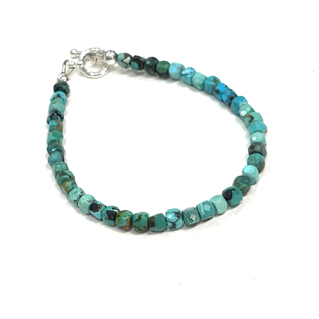Top-grade Turquoise faceted cubed  beads strung on durable Beadalon wire with a sterling silver toggle on a white background  front left angle view. 