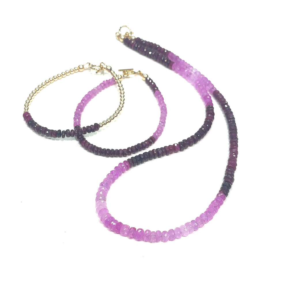 Two genuine ruby gemstone beaded bracelets with gold-filled toggle clasps, featuring faceted roundel rubies ranging in color from purple to red, on a white background front overview with its matching necklace.