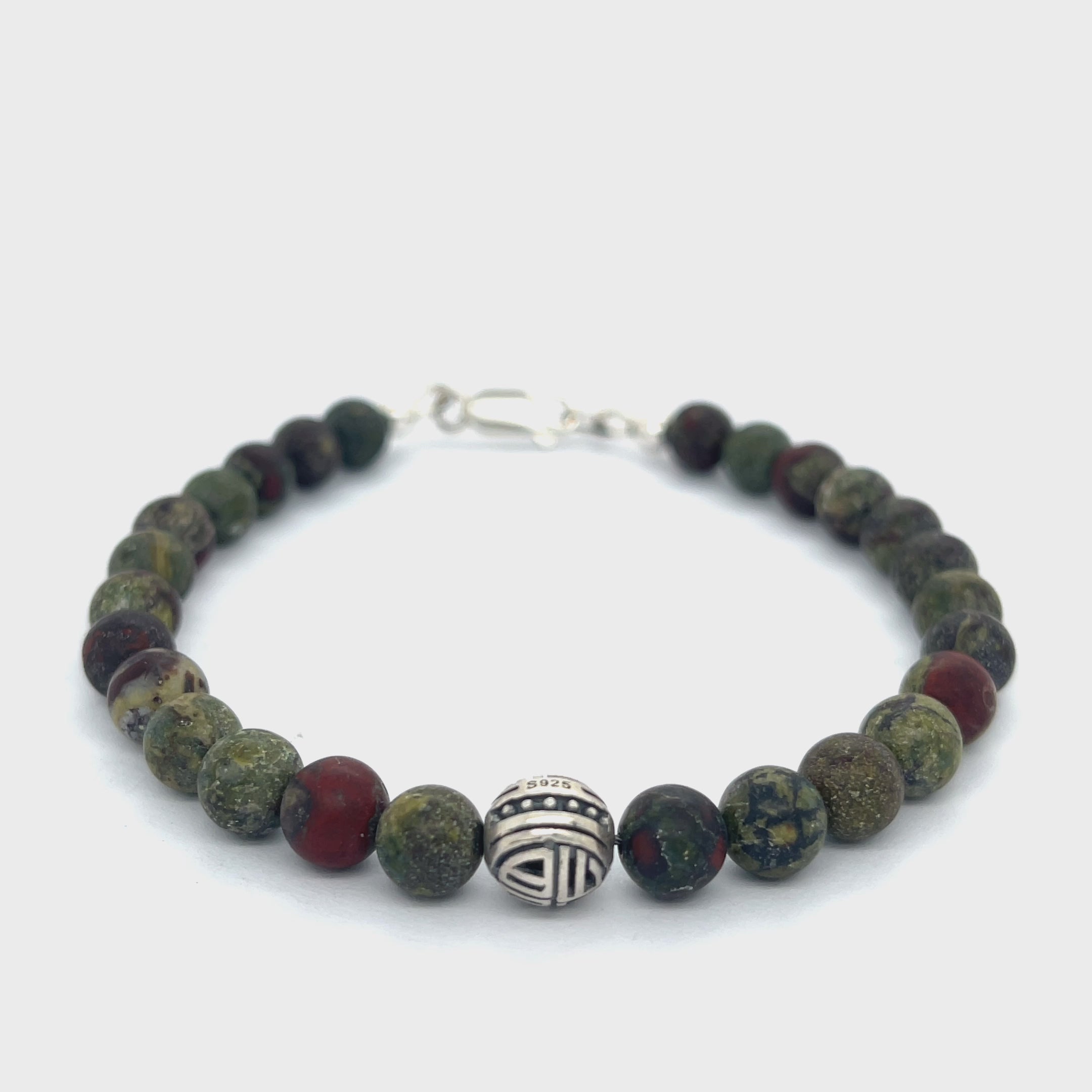 Dragon Blood Jasper gemstone beaded bracelet with sterling silver pattern bead and a lobster claw clasp showing red and green natural patterns  on a white background, front view.  video