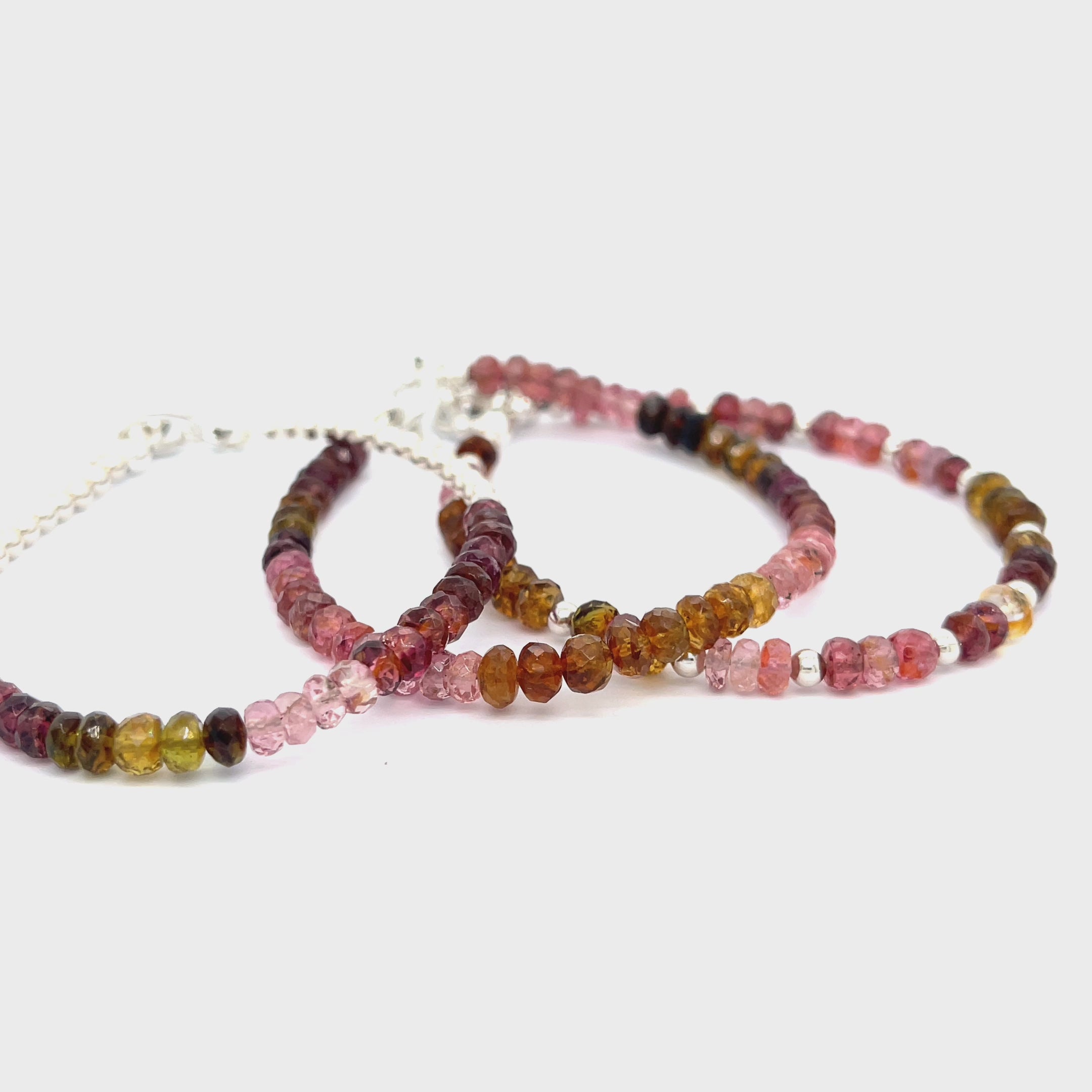 A series of beaded bracelets featuring tourmaline gemstones in various shades of pink, brown, and green, with sterling silver accents and a silver toggle on a white background, front and center overview. video