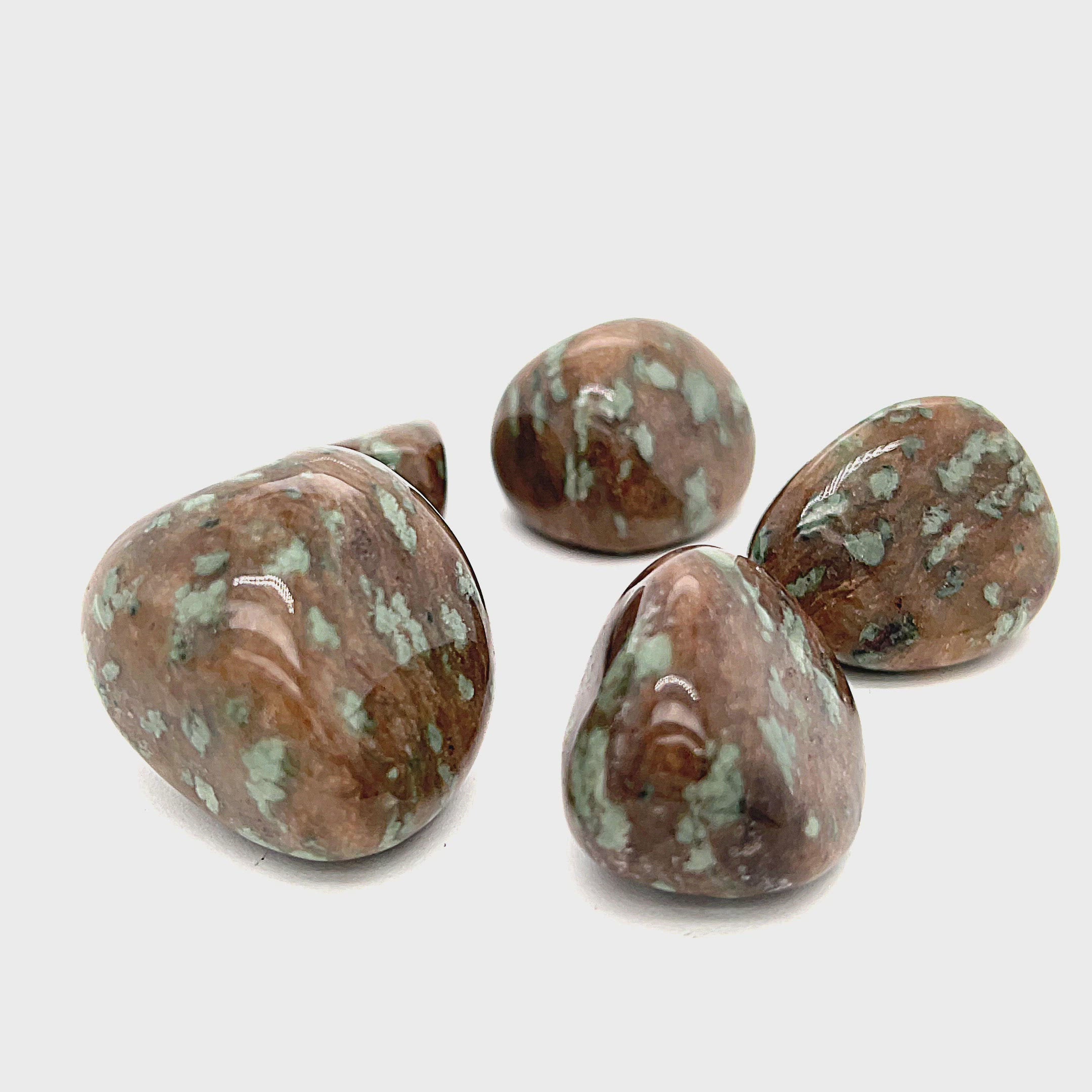 A collection of tumbled Nundoorite gemstones with a brown base and green speckled patterns displayed on a white background, overview. video