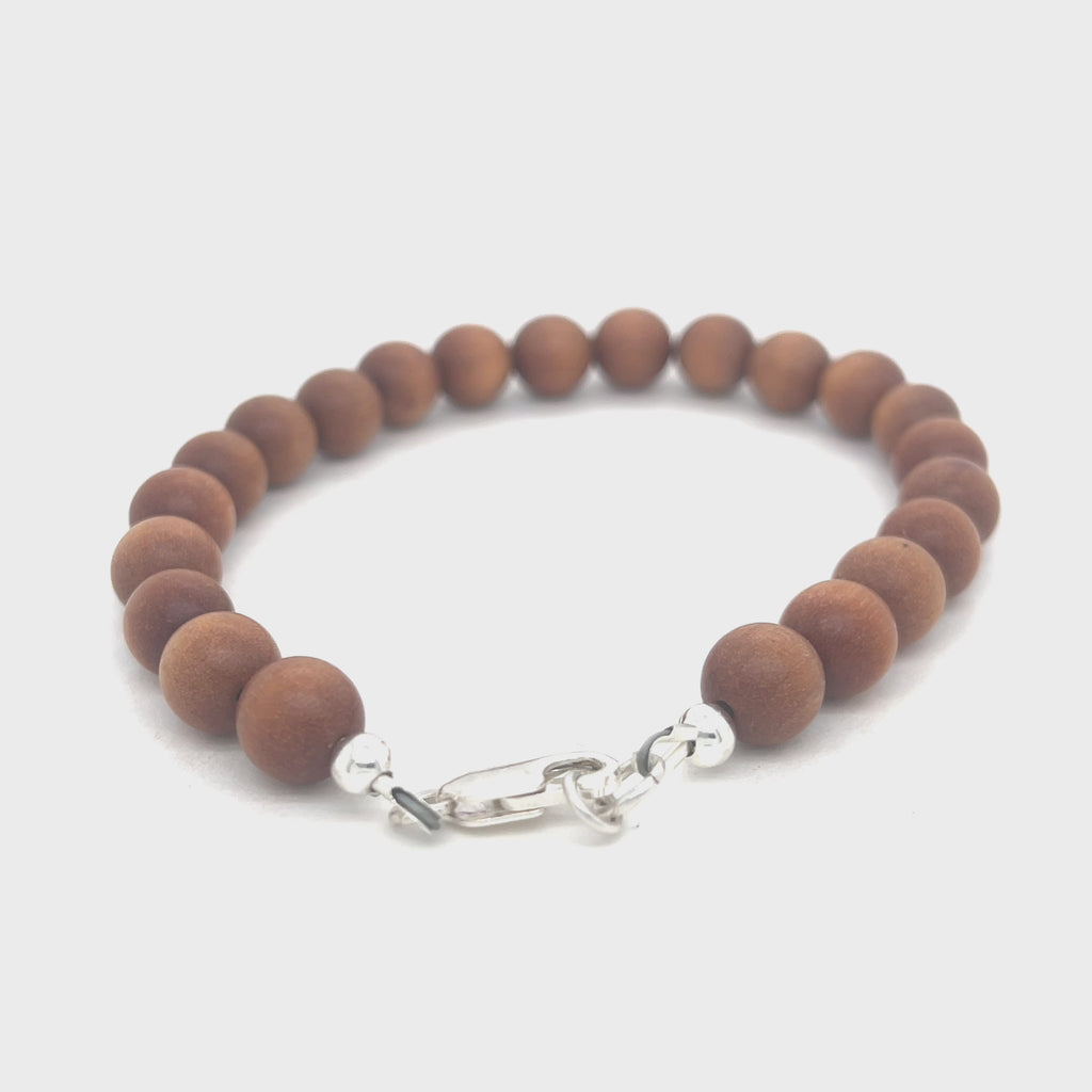 A brown sandalwood beaded bracelet with a sterling silver lobster-claw clasp on a white background, front view. video