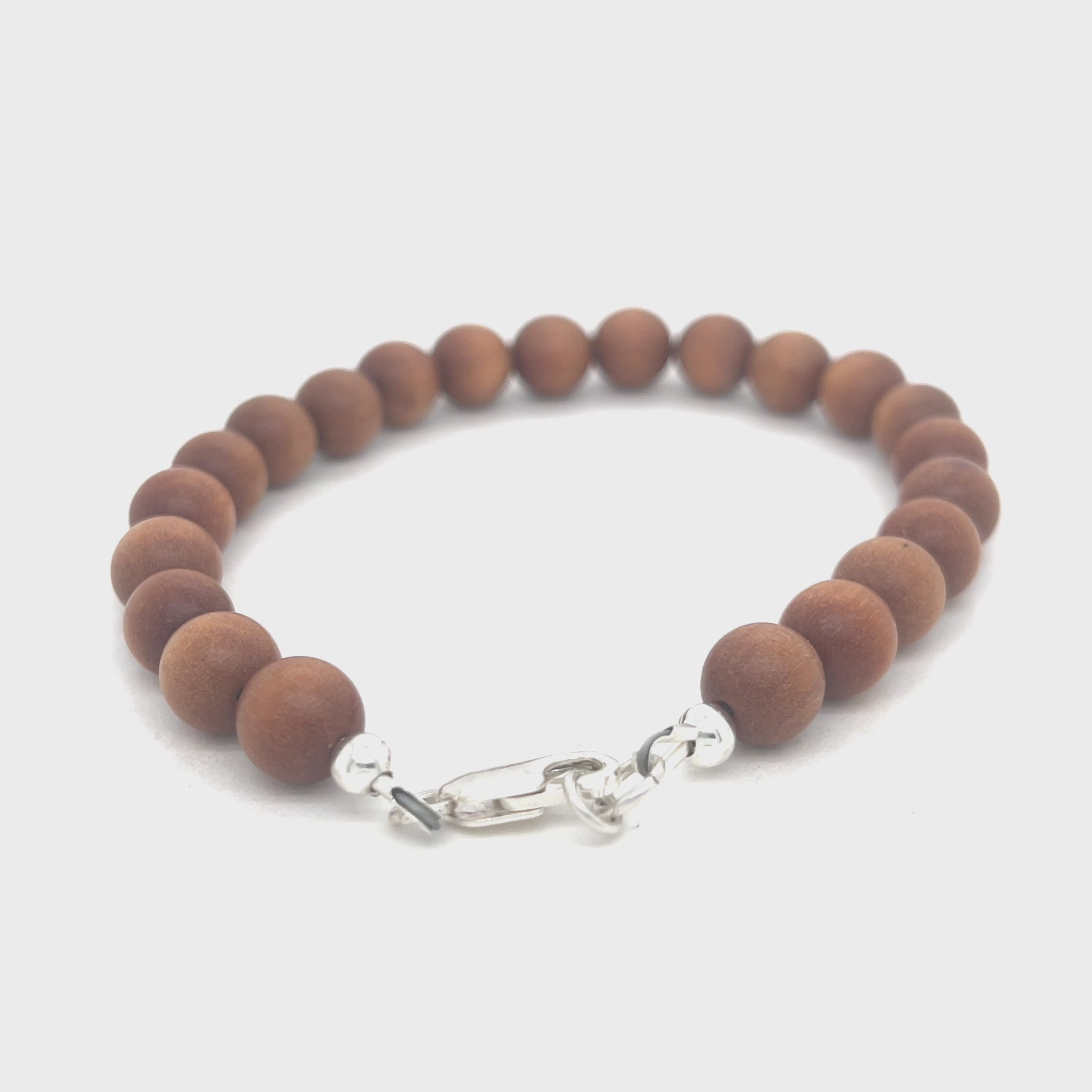 A brown sandalwood beaded bracelet with a sterling silver lobster-claw clasp on a white background, front view. video