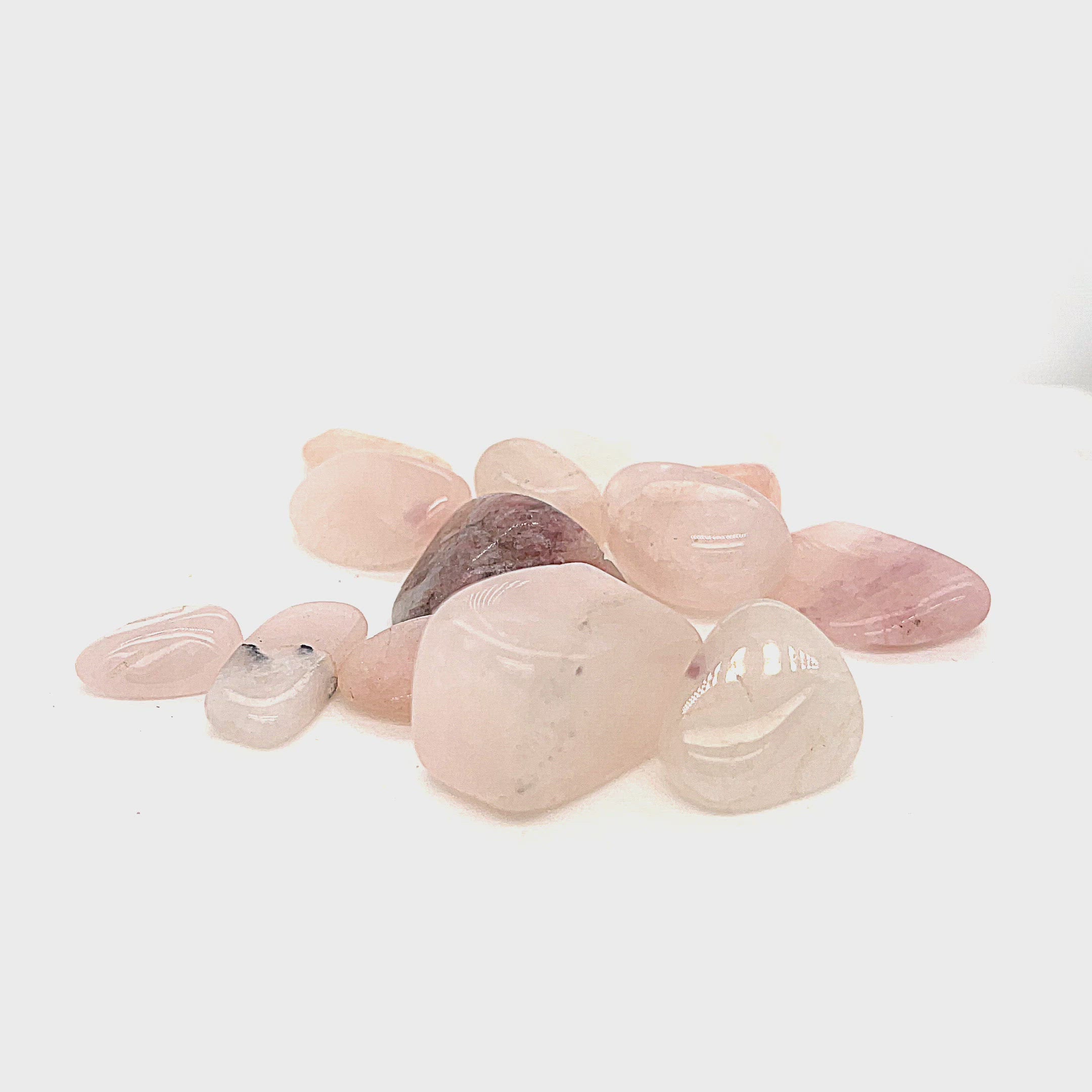 A collection of xs tumbled Petalite gemstones with a pink hue, displayed on a white background, front overview. video