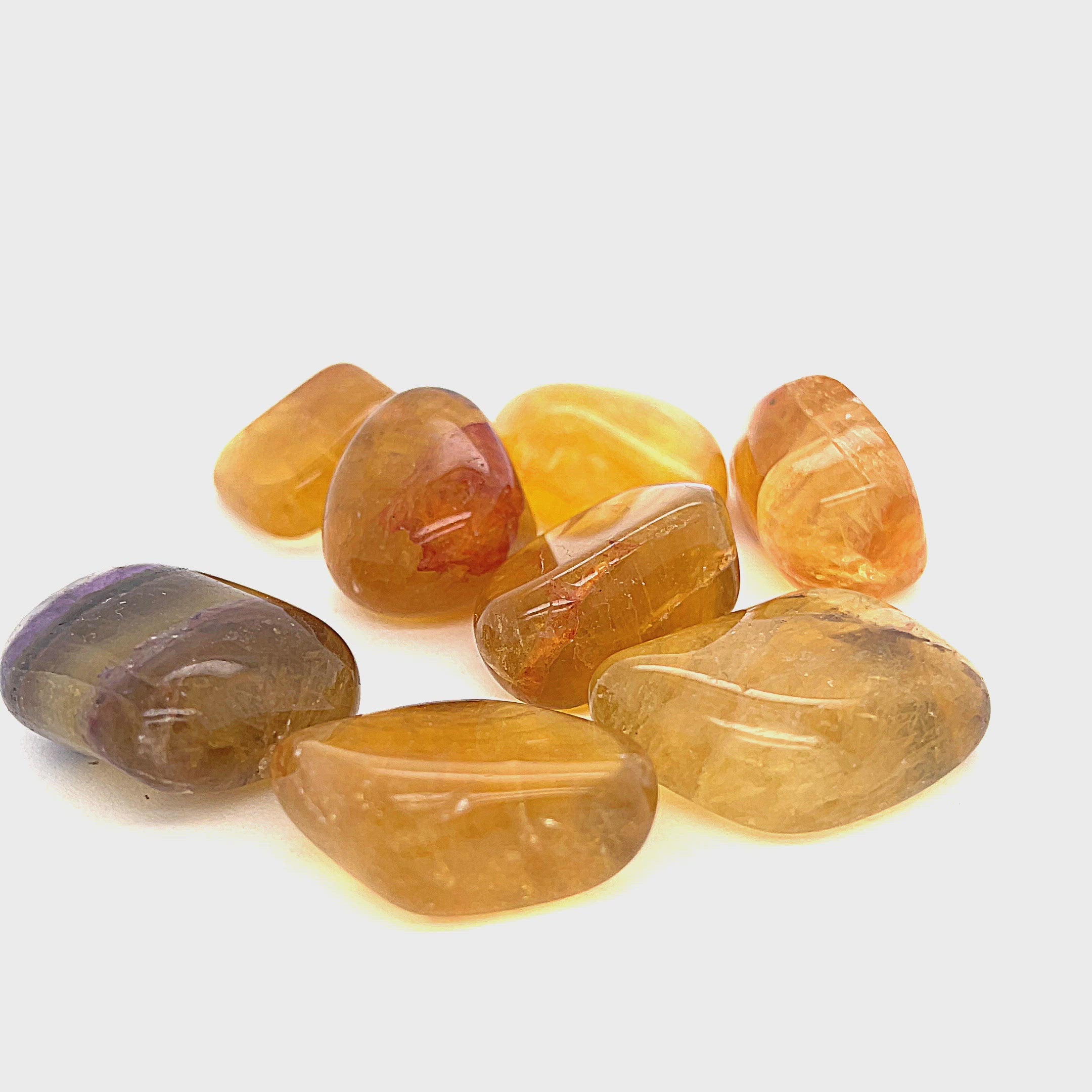 A collection of Yellow Fluorite tumbled gemstones displayed on a white surface, front overview. video