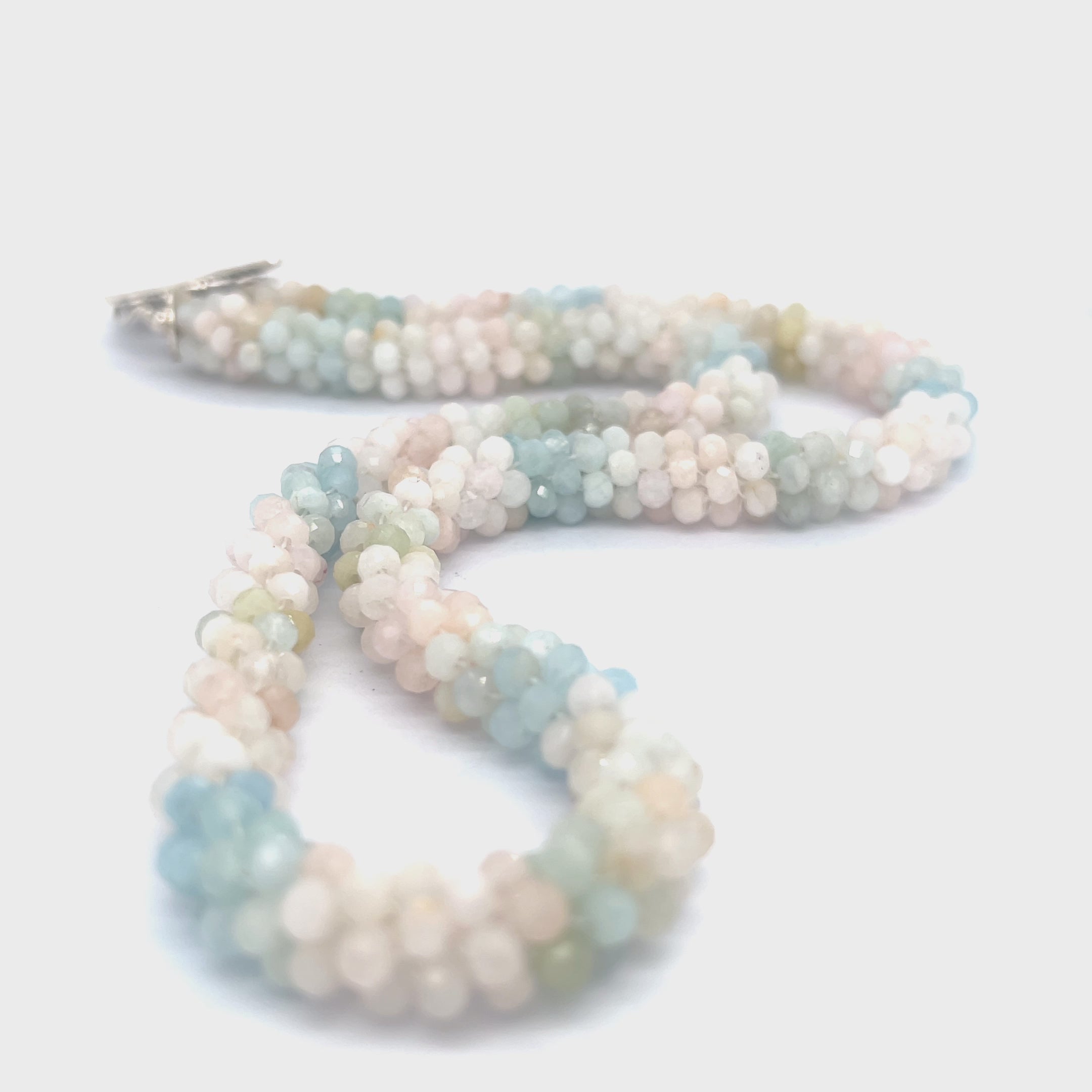A crocheted morganite gemstone necklace with a variety of colorful beads and a sterling silver decorative toggle on a white background, center overview. video