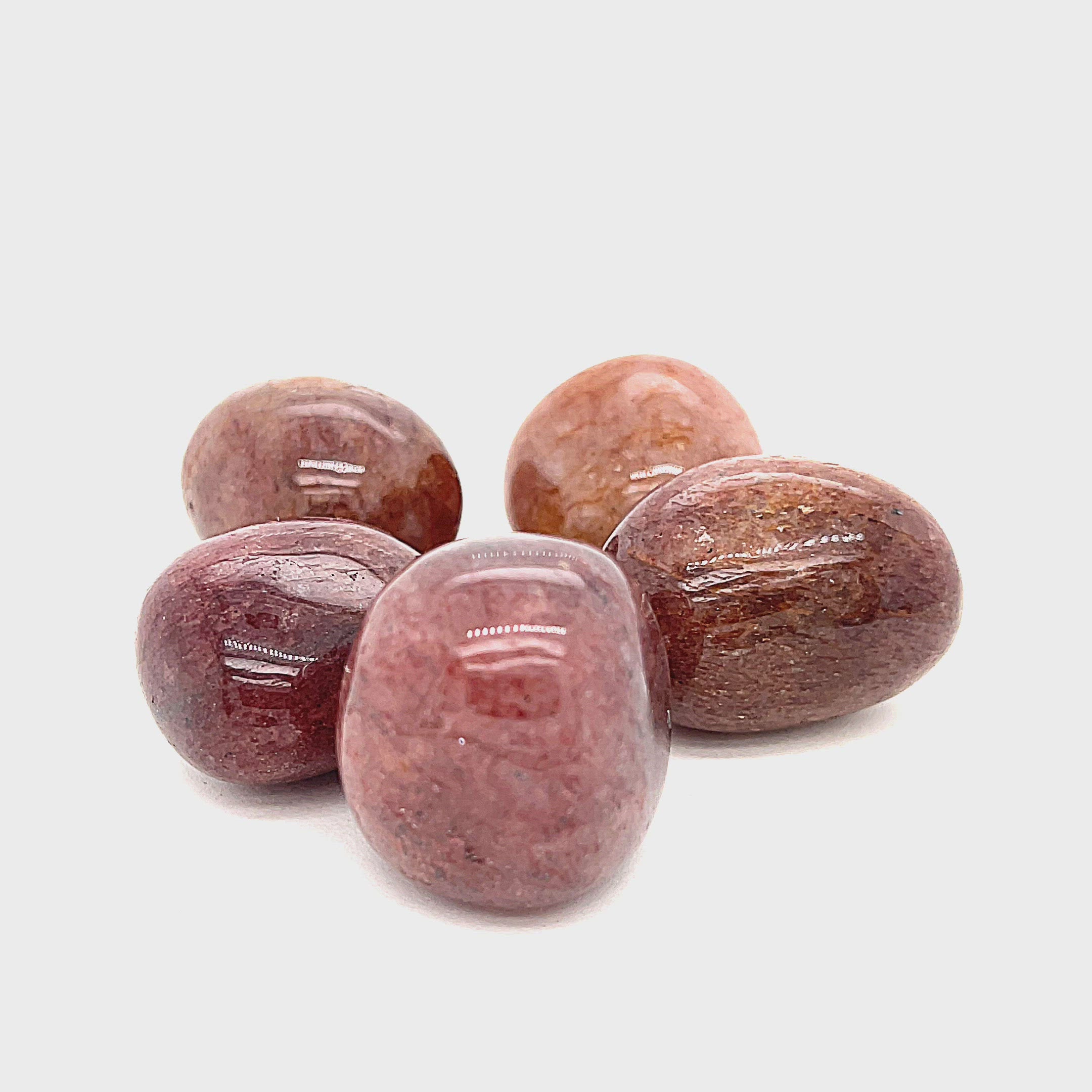 A collection of round Muscovite tumbled gemstones with a smooth, polished surface in shades of red and brown on a white background, front overview. video