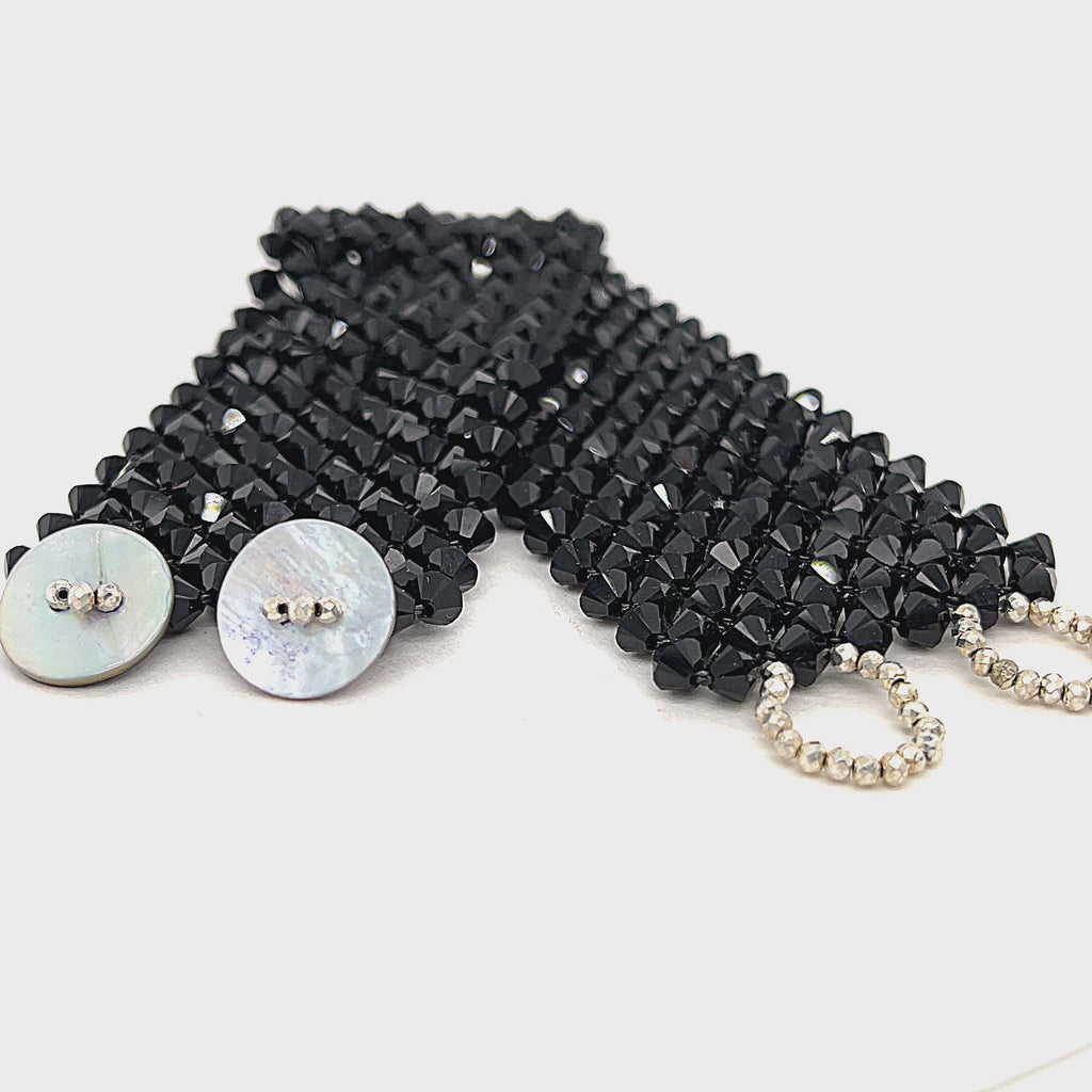 A black colored Swarovski crystal cuff bracelet with abalone shell and silver-coated pyrite buttons at the center front view on a white background. video