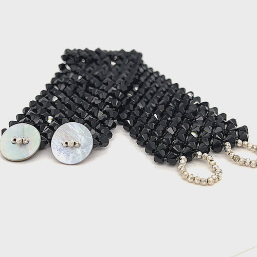A black colored Swarovski crystal cuff bracelet with abalone shell and silver-coated pyrite buttons at the center front view on a white background. video