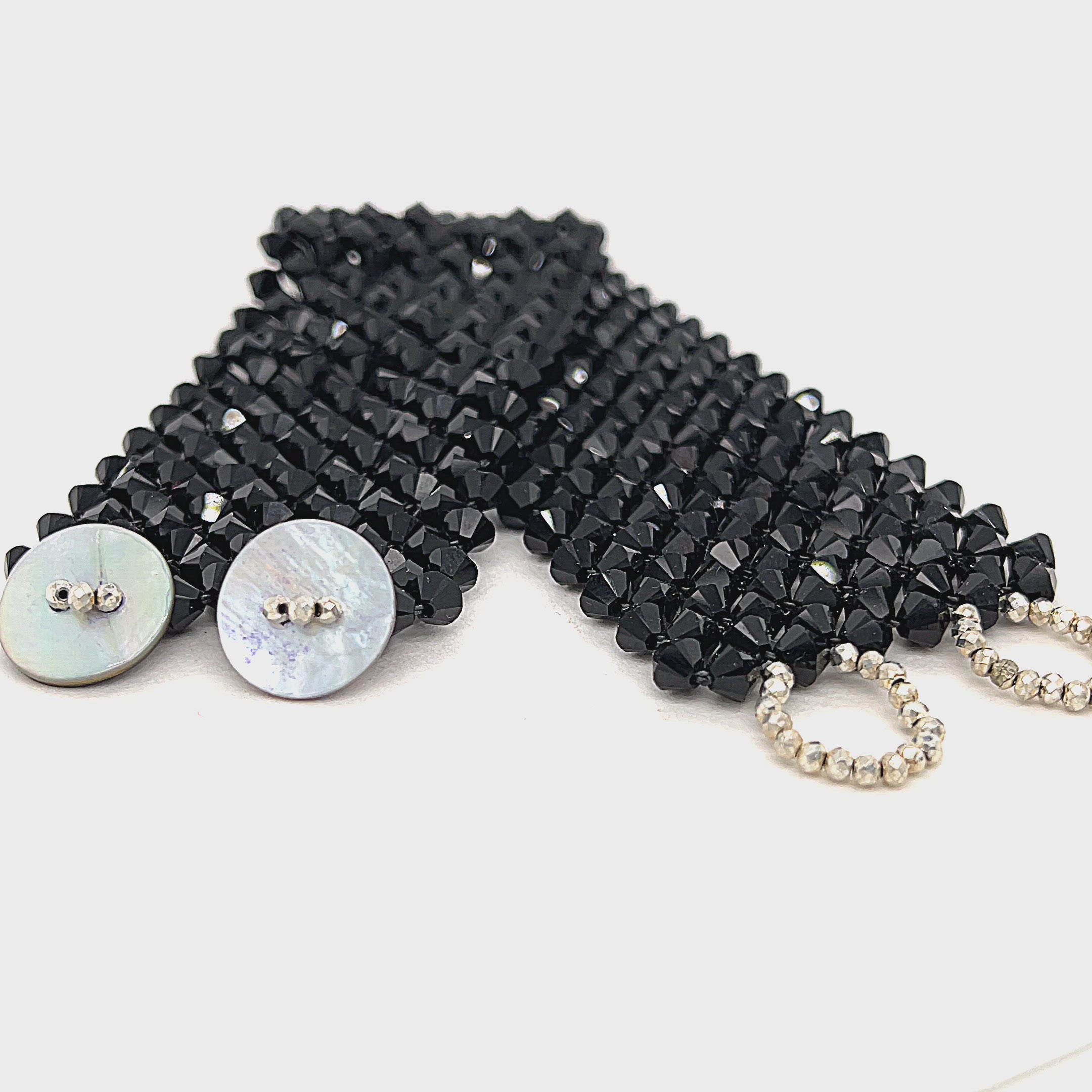 A black colored Swarovski crystal cuff bracelet with abalone shell and silver-coated pyrite buttons at the center front view on a white background. video