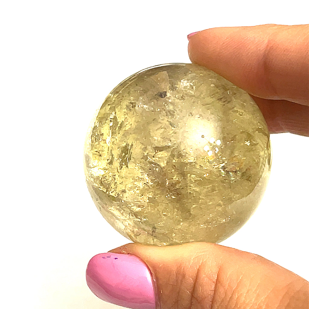 one  citrine gemstone sphere in the models finger tips on a white background for a close up view.