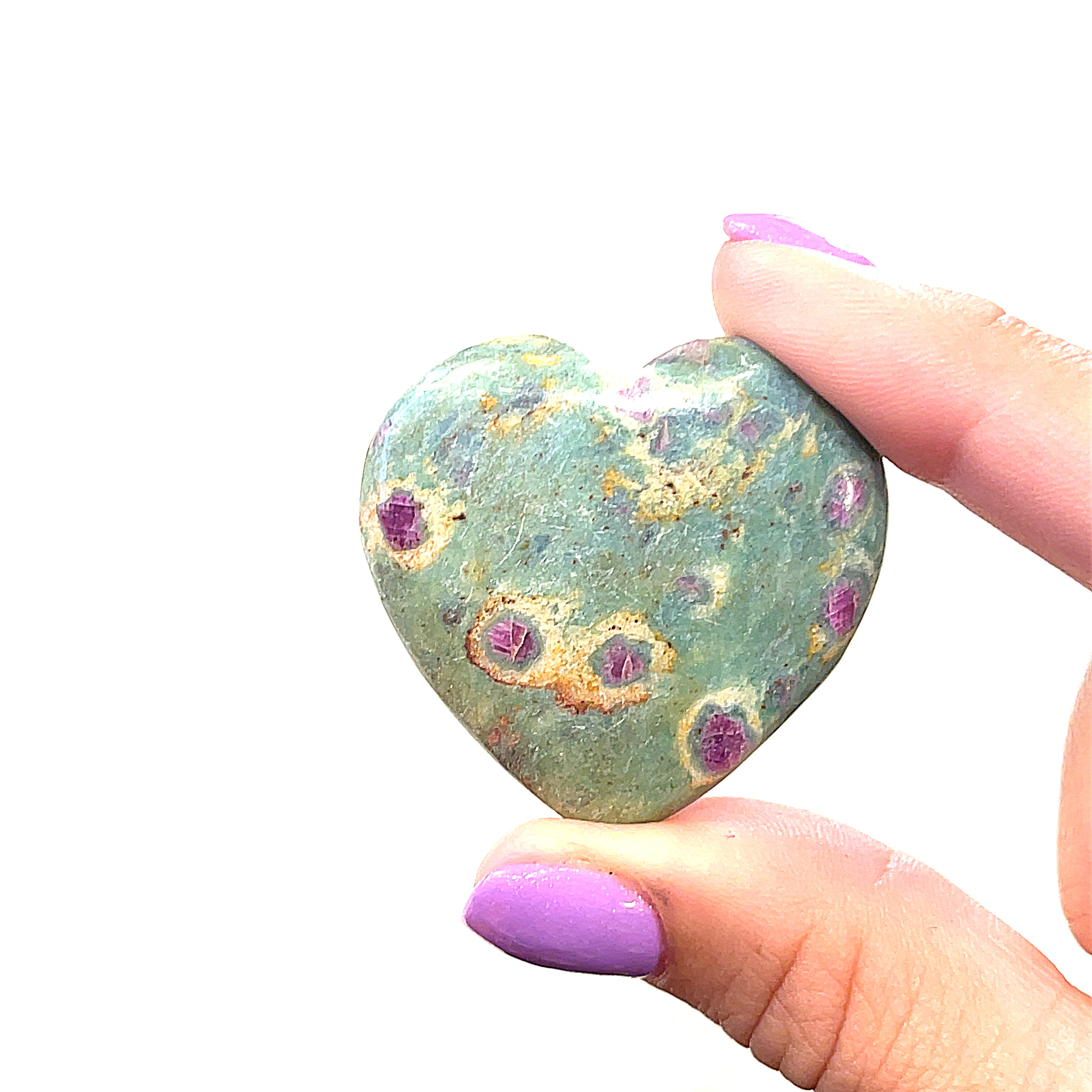 one heart-shaped Ruby Fuchsite gemstone carvings displayed in a models fingertips  on a white background front overview.